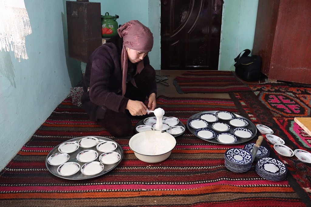 A woman in an Uzbek home spooning nisholda, the whipped Ramadan sweet, into bowls before iftar